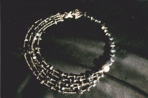 Ras de cou assymétrique avec un côté du 1/3 du collier enfilé de grosses perles d'hématites cubiformes, terminé par une grosse perles argent avec motifs puis plusieurs rangs de rocaille anthracite et petites hématites sur les 2/3 restants