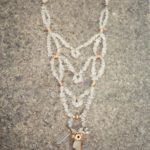 Grand collier plastron avec plusieurs rangs de perles de cristal de roche, terminé par un pendant avec un gros cristal de roche brut cerclé de laiton et fleurs de laiton
