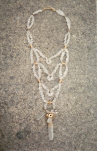 Grand collier plastron avec plusieurs rangs de perles de cristal de roche, terminé par un pendant avec un gros cristal de roche brut cerclé de laiton et fleurs de laiton