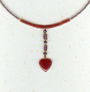 Collier ras de cou et son pendant central finissant avec un coeur en cornaline rouge, le tout enfilé avec des petites perles rondes de grenats et petites cornalines tubes