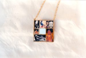 Sautoir avec un gros pendentif carré avec un petit miroir carré au centres et images de femmes de magazines découpés disposées autour, et recouvertes de résine, le tout dans un serti en laiton