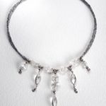 collier petit plastron son tour de cou en mini perles de rocaille gris hématites, perles forme baroque de cristal de roche, et 5 pendants avec cabochon forme amande de cristal de roche sertis.