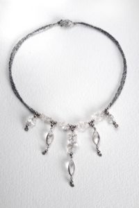 collier petit plastron son tour de cou en mini perles de rocaille gris hématites, perles forme baroque de cristal de roche, et 5 pendants avec cabochon forme amande de cristal de roche sertis.