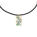 Création pendentif rectangle en laiton avec motif de feuille stylisée ajourée et patinée vert, l'encadrement doré, monté sur tour une tresse de cuir fine noire.