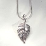 Pendentif création pièce unique d'une feuille en argent toute gravée de nervures et son pétiole accroché sur la chaîne