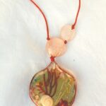 Pendentif résine forme organique sur cordon de soie rouge avec inclusion de feuille eucalyptus, coquillages, strass, pétale de rose, gorgone rouge, personnage en fil laiton, le tout représentant un paysage de songe