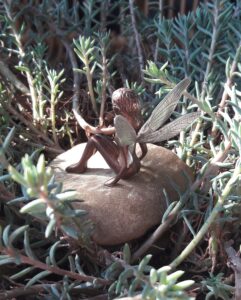 Petite fée en bronze de 3,2 cm aux ailes de libellule en argent gravées au burin, assise et soclée sur un caillou ramassé.